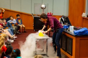 Kids watch Dr. Tatiana pour liquid nitrogen onto a balloon.